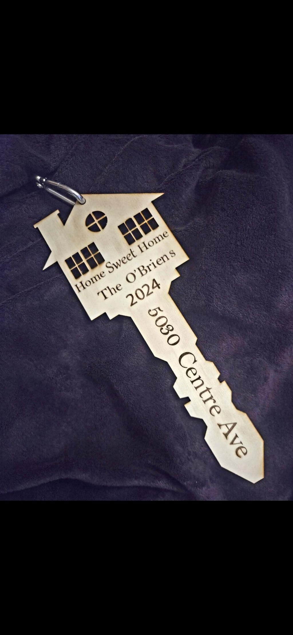 Decorative key-shaped house ornament with engraved text on a purple fabric background